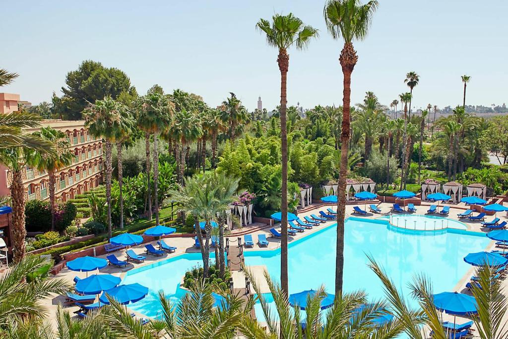 马拉喀什美丽典费斯酒店的享有带蓝伞和棕榈树的游泳池的顶部景致