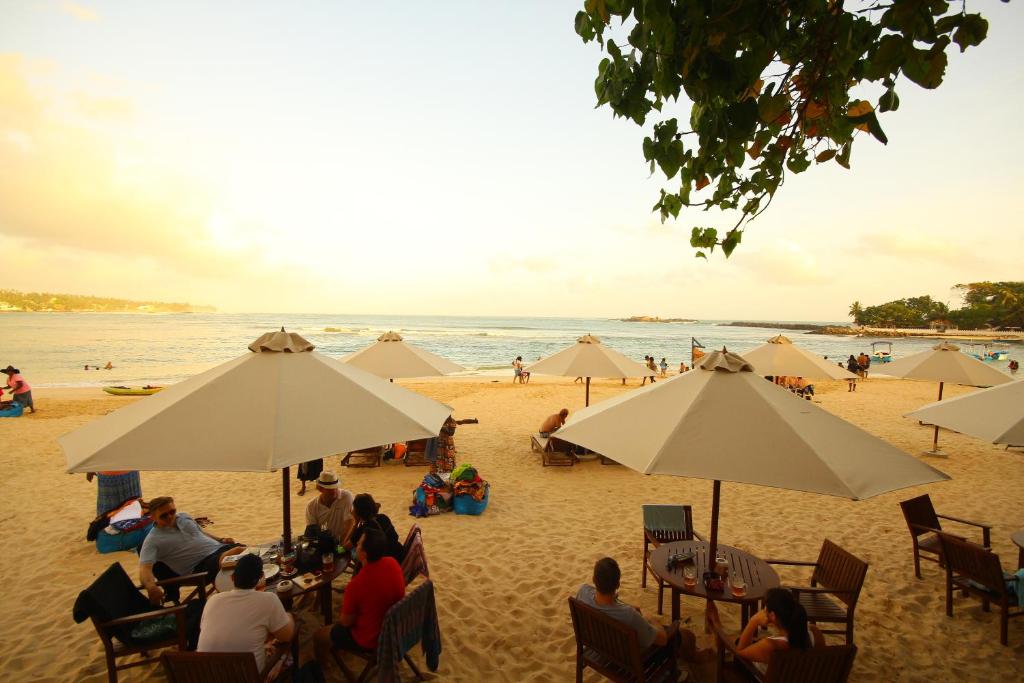 乌纳瓦图纳翠鸟酒店的一群人坐在海滩上的伞下