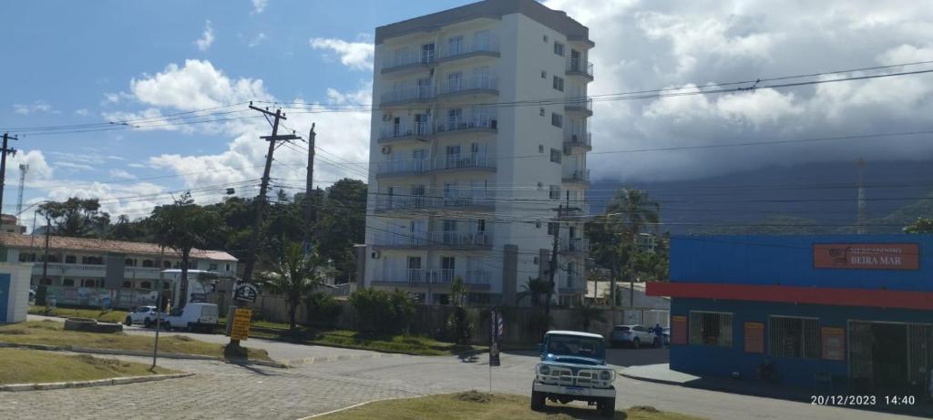 卡拉瓜塔图巴Riviera Massaguaçu 23的一座高大的白色建筑,前面有一辆汽车