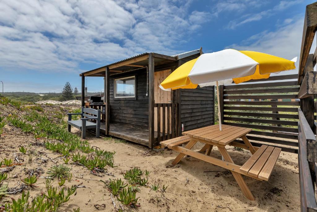 AwanuiKaro Hut B - Ninety Mile Beachfront Cabin的海滩上的野餐桌和遮阳伞