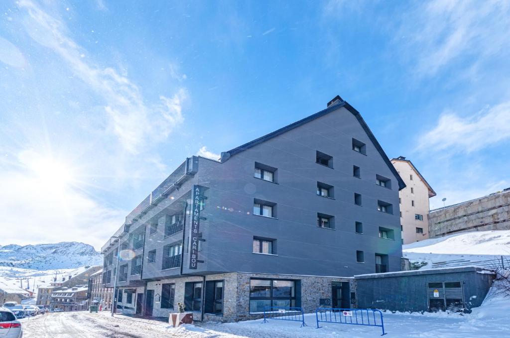 帕斯底拉卡萨Apartamentos Caribou的雪中的一个建筑,太阳在后面