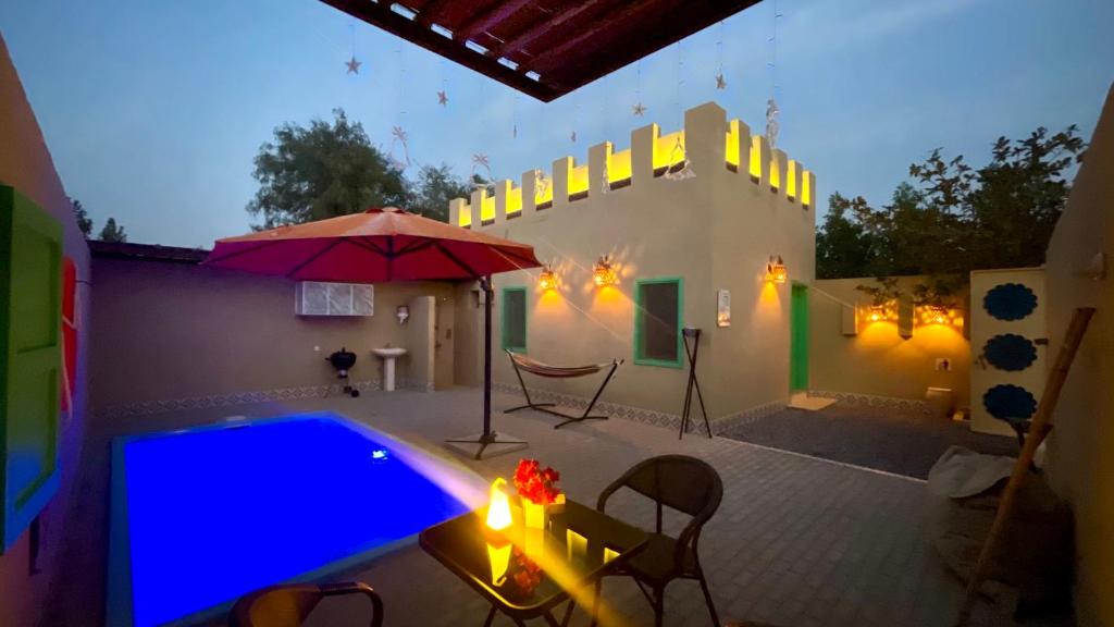 Al ḨamrānīyahAl Bait resort with private swimming pools -HRS stables的一个带游泳池、遮阳伞和桌子的庭院