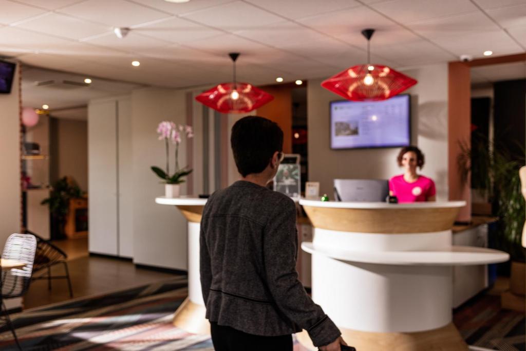 拉沃尔ibis Styles Toulouse Lavaur的一名年轻人在柜台上与一名妇女一起走在大厅里