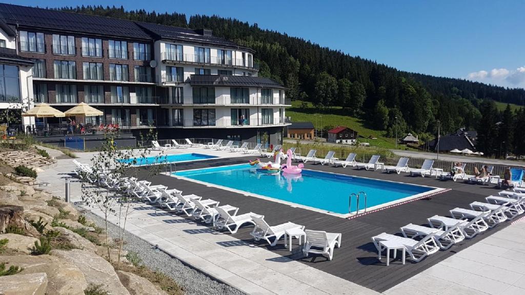 西恩纳Czarna Perła - Czarna Góra Resort by Sun & Snow z nielimitowanym basenem的一个带椅子的游泳池和一个度假村