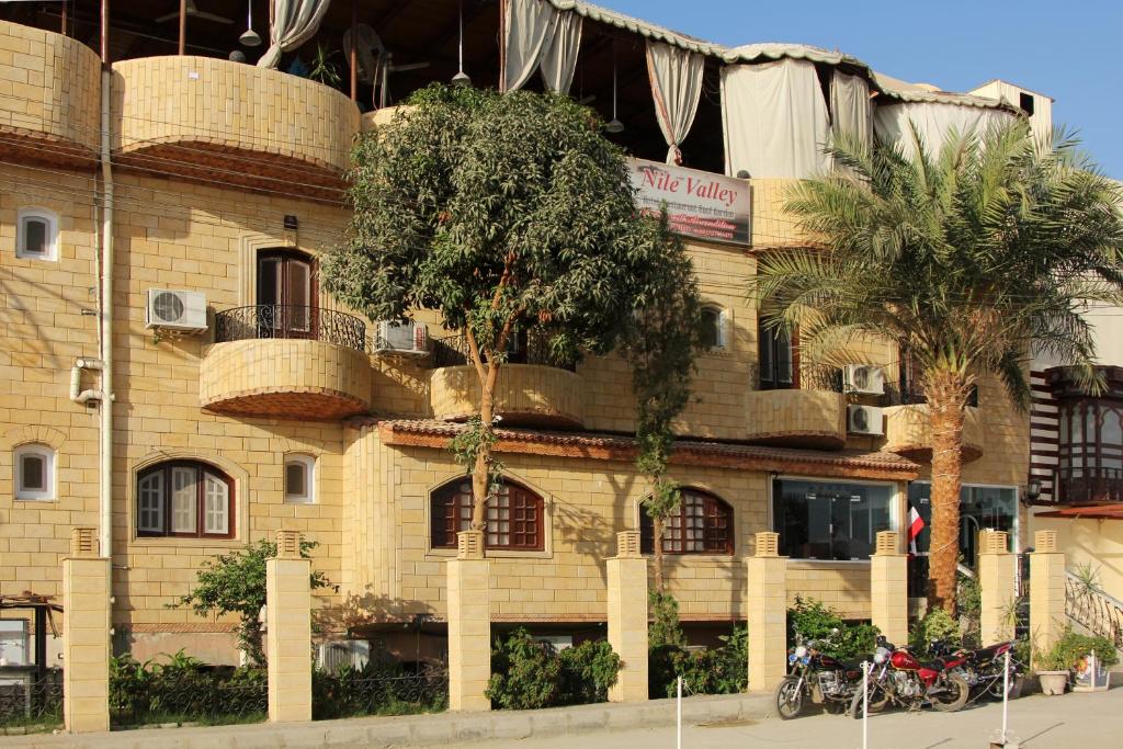 卢克索尼罗河谷酒店的一座黄色的砖砌建筑,前面有棕榈树