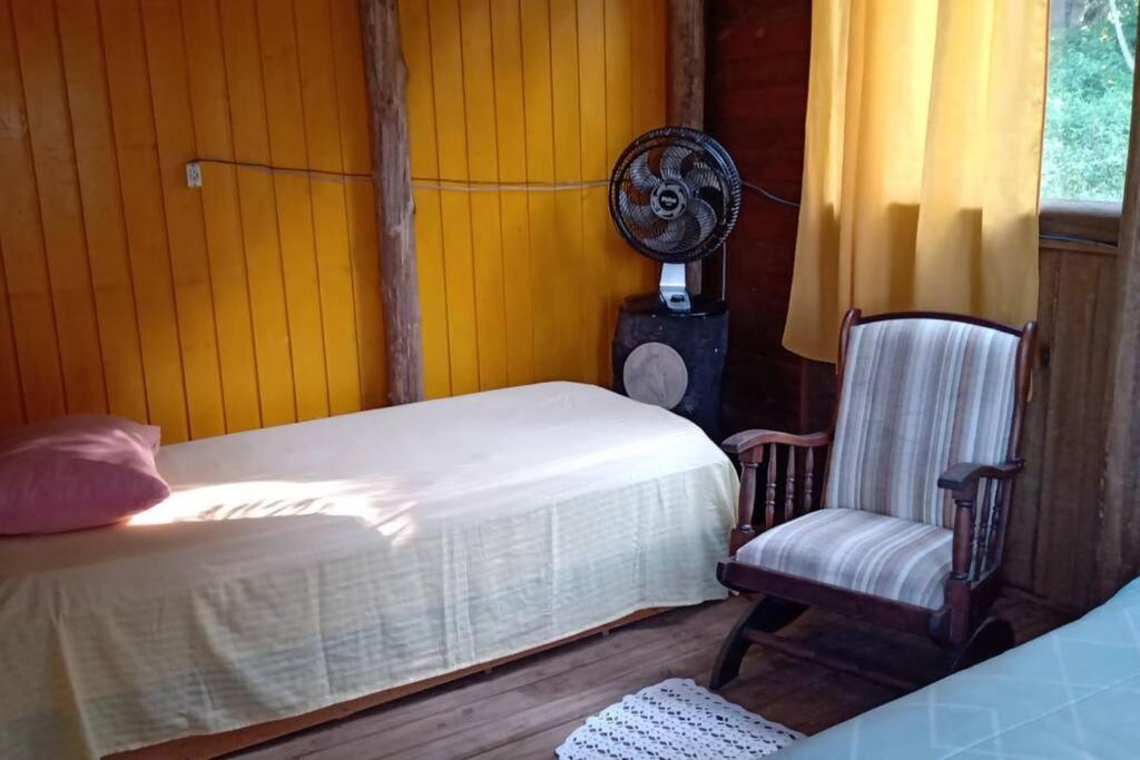 圣阿马鲁-达因佩拉特里斯Casa rústica pertinho das águas的一间卧室配有一张床、一把椅子和风扇