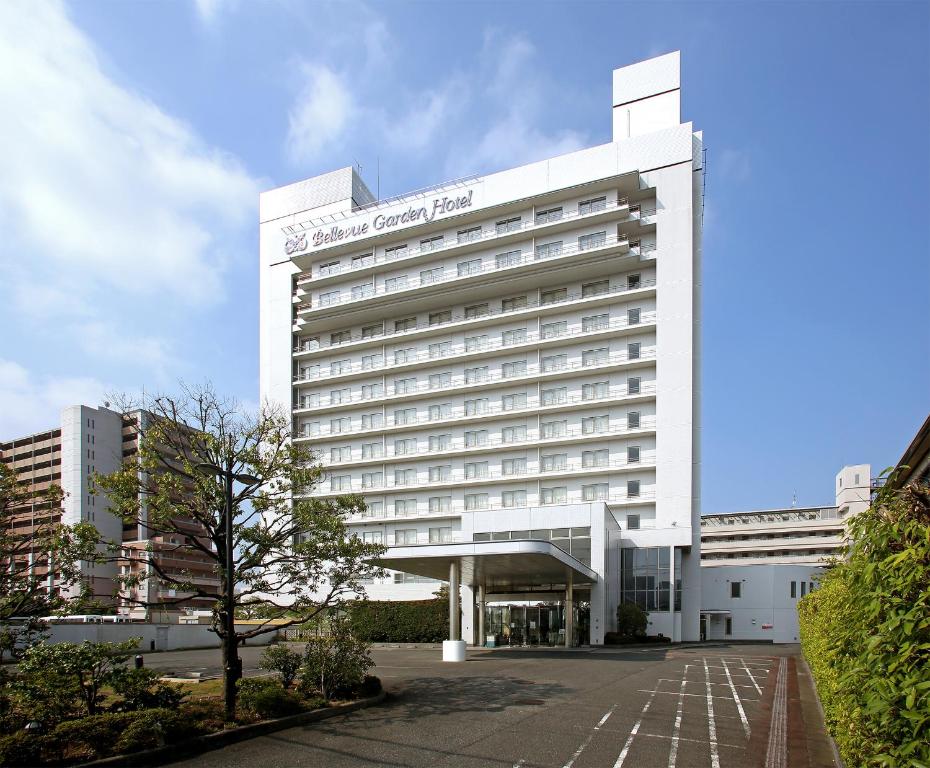 泉佐野關西機場美景花園飯店的一座白色的酒店建筑,前面有一棵树