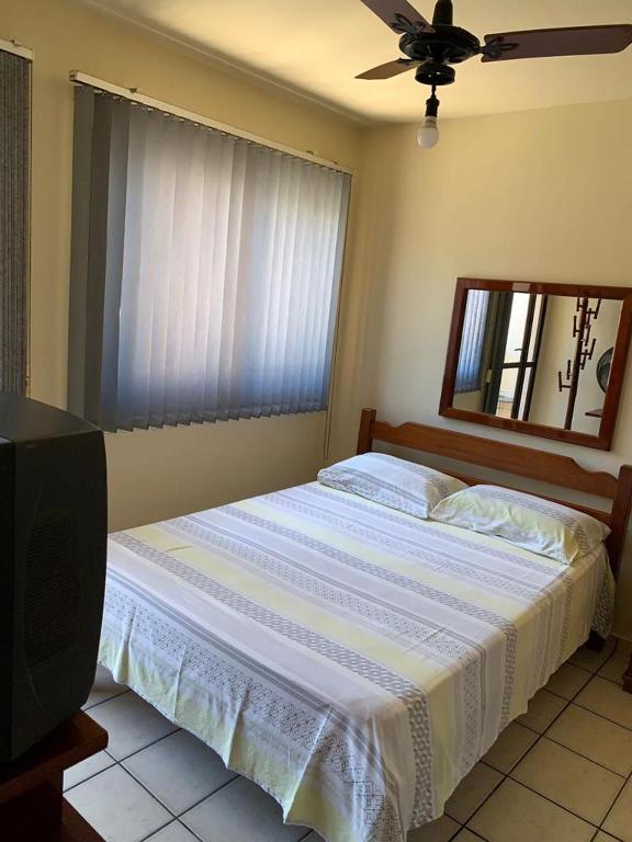 瓜拉派瑞APTO PRAIA DO MORRO, 02 QUARTOS C SUITE, WI-FI, GARAGEM, 1 ANDAR ESCADA.的一间卧室配有一张带吊扇的床和一台电视。