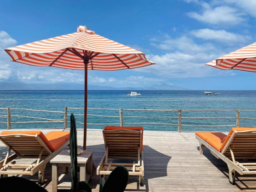 珀尼达岛VnS Beachfront Guesthouse的一个带椅子和遮阳伞的甲板和大海