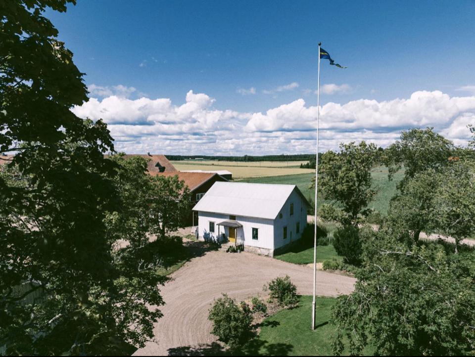 克里斯蒂娜港Åkerbo gård charmigt renoverad flygel的一块带旗帜的田野中间的白色房子