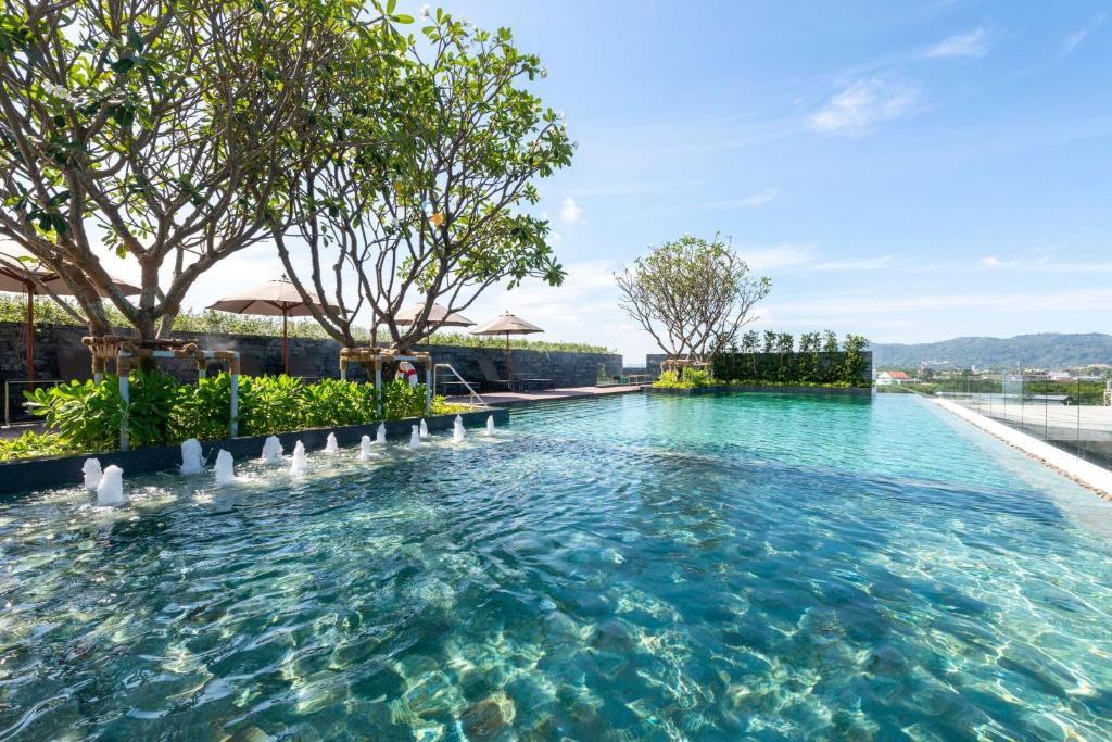 普吉镇Ramada Plaza by Wyndham Chao Fah Phuket的拥有蓝色海水和树木的游泳池