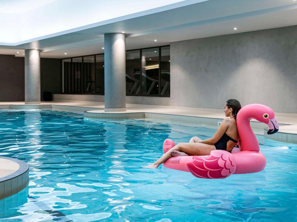 鲁瓦西昂法兰西普尔曼巴黎戴高乐机场酒店的坐在游泳池里的粉红色火烈鸟的女人