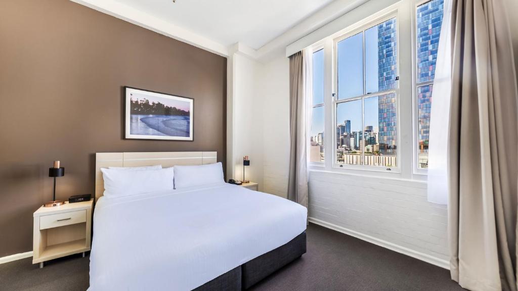 悉尼Oaks Sydney Goldsbrough Suites的卧室设有白色的床和大窗户