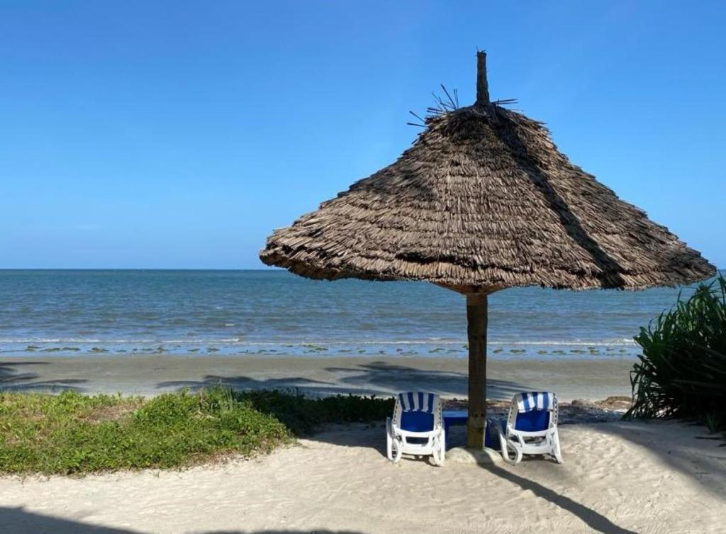 MkwajaBarry's Beach Resort的海滩上的两把椅子和一把草伞
