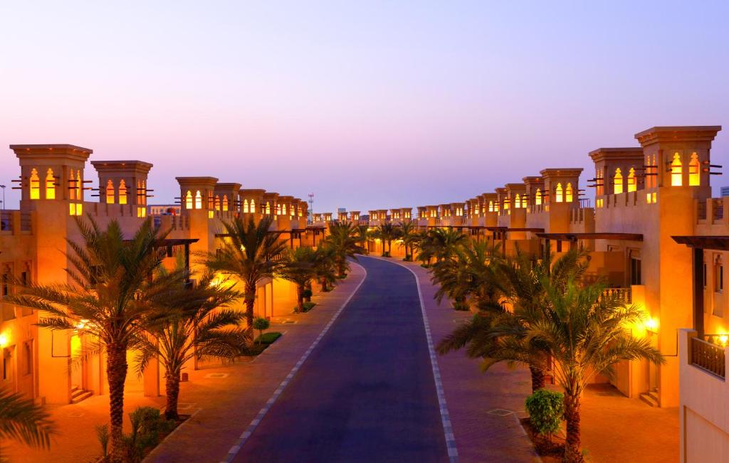 拉斯阿尔卡麦Al Hamra Village Hotel的一条棕榈树成荫的街道,晚上的建筑