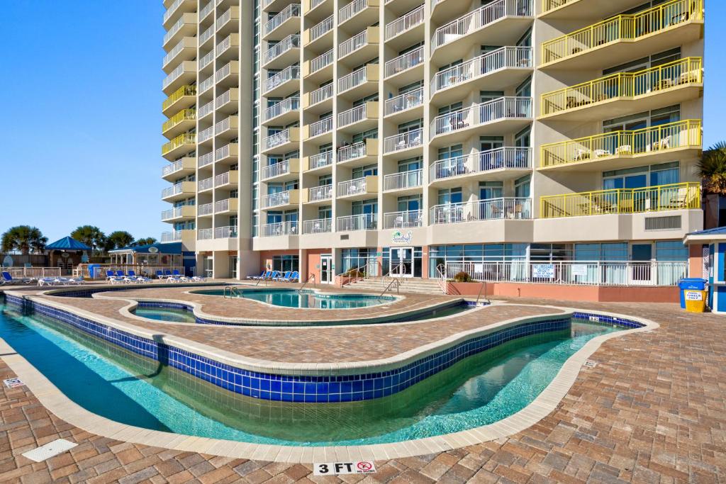 默特尔比奇Bay Watch Resort的一座大型公寓楼,前面设有两个游泳池