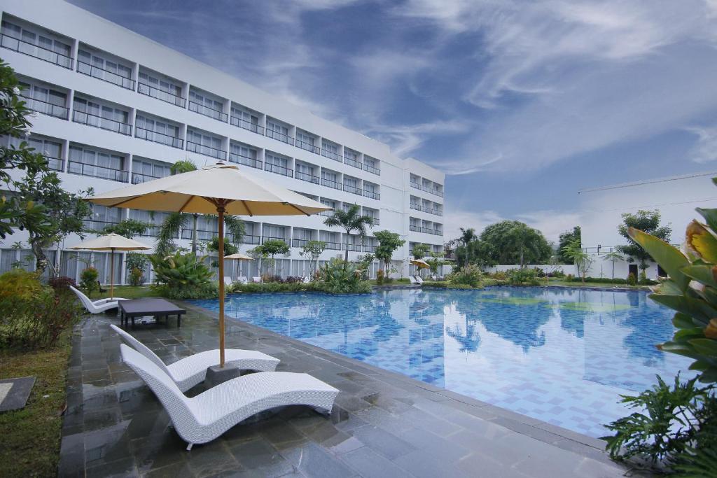龙目岛库塔Raja Hotel Kuta Mandalika Resort & Convention的酒店设有一个大型游泳池,游泳池内摆放着椅子和遮阳伞。