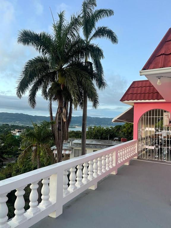 蒙特哥贝Three Palm Villa的一个带棕榈树和粉红色房子的阳台