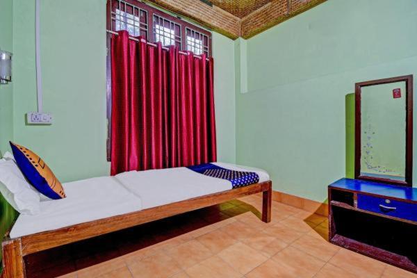 焦尔哈德Ashrayaa Prakreeti.的一间卧室配有一张带红色窗帘的床和一台电视。