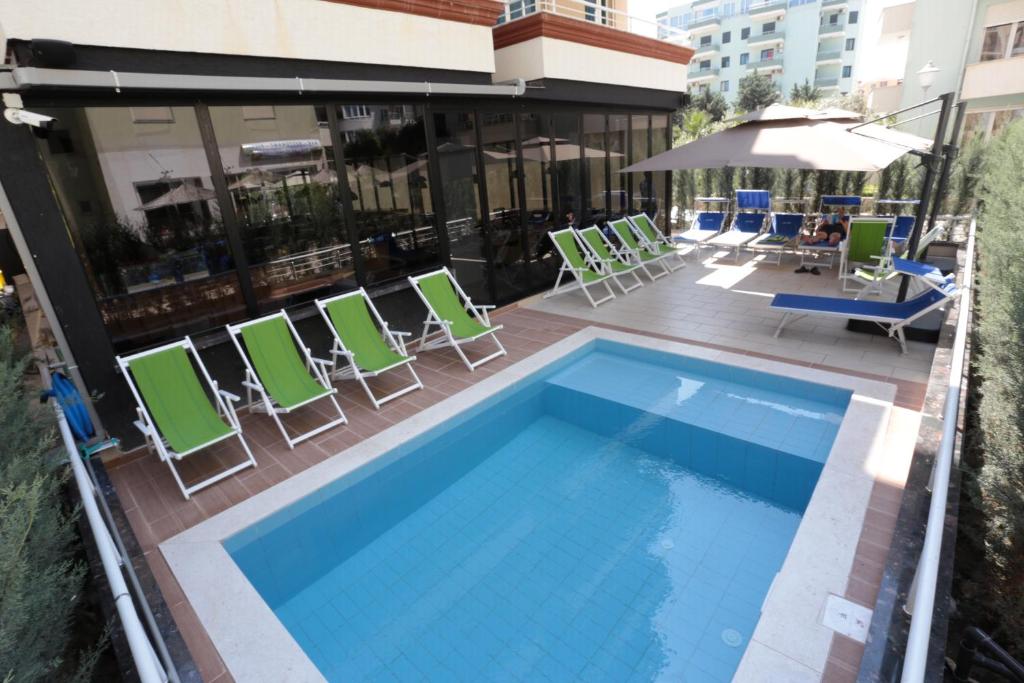 都拉斯Alvin Comfort Hotel的一个带椅子和遮阳伞的阳台的游泳池
