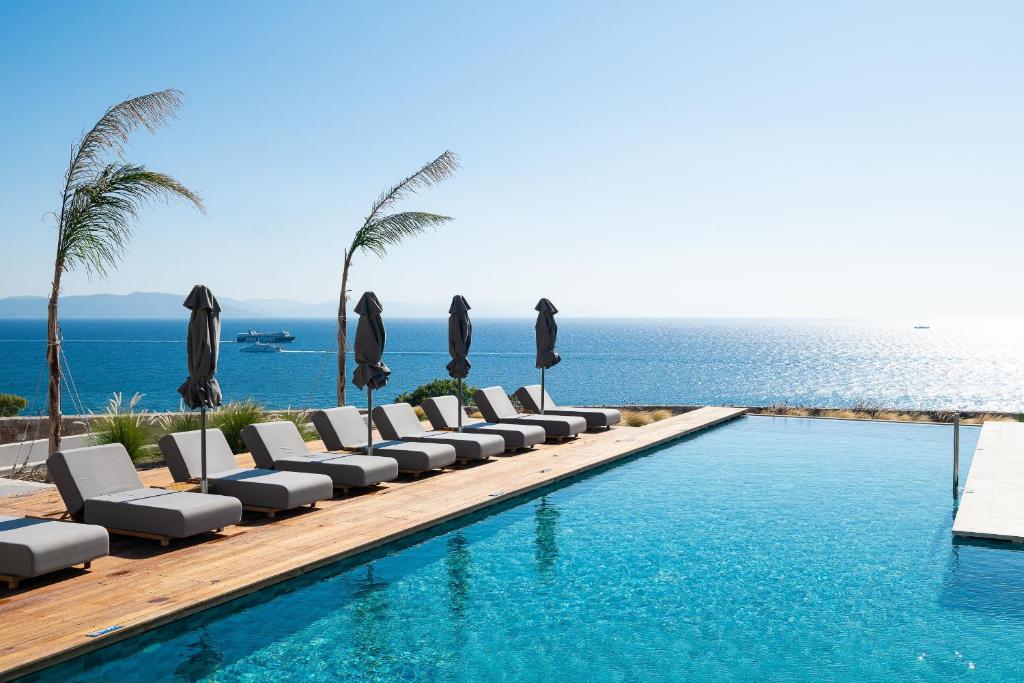Ágios FokásKOIA All - Suite Well Being Resort - Adults Only的毗邻大海的带椅子和遮阳伞的游泳池