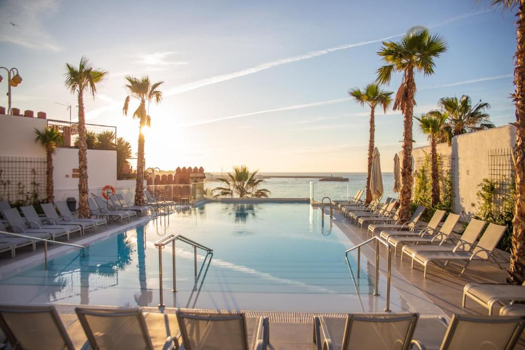 贝纳尔马德纳Hotel Benalmadena Beach的一个带椅子的游泳池,棕榈树