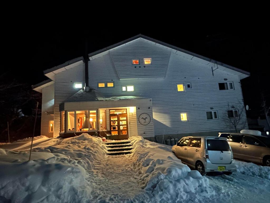 饭山市Raicho Lodge Madarao的雪中停放汽车的房子