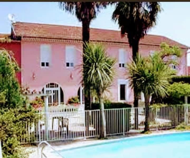 Laroque-dʼOlmesLe Castel d'olmes的一座粉红色的房子,里面种有棕榈树,设有围栏