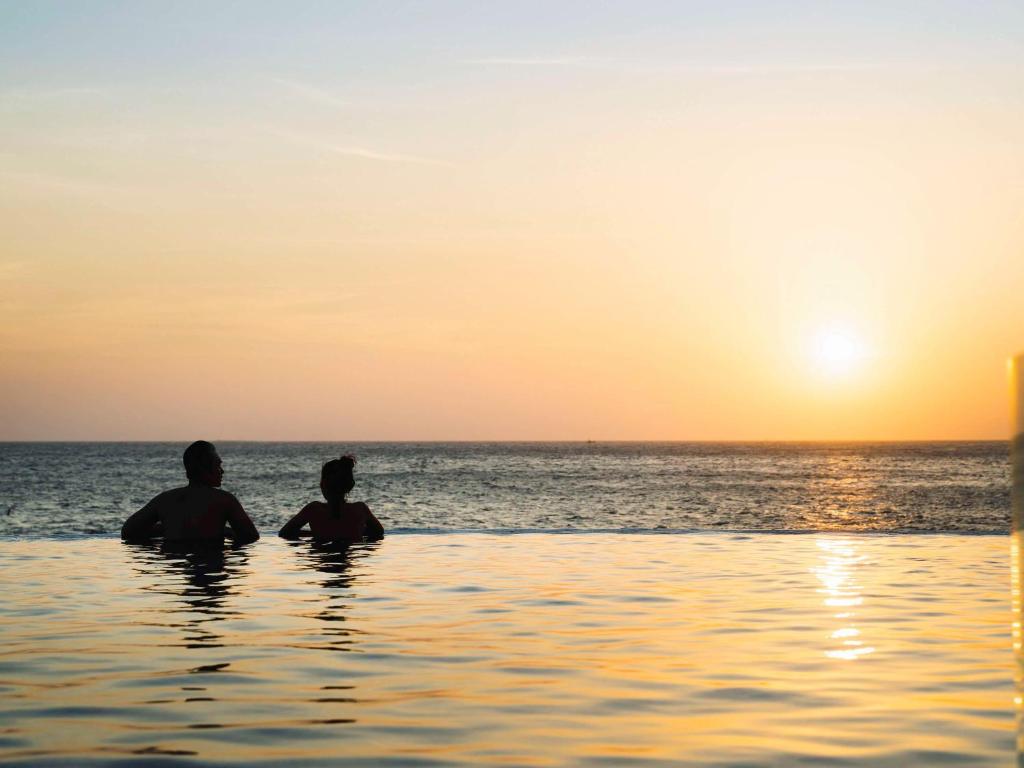 头顿Mercure Vung Tau Resort的两人坐在海洋里,欣赏日落