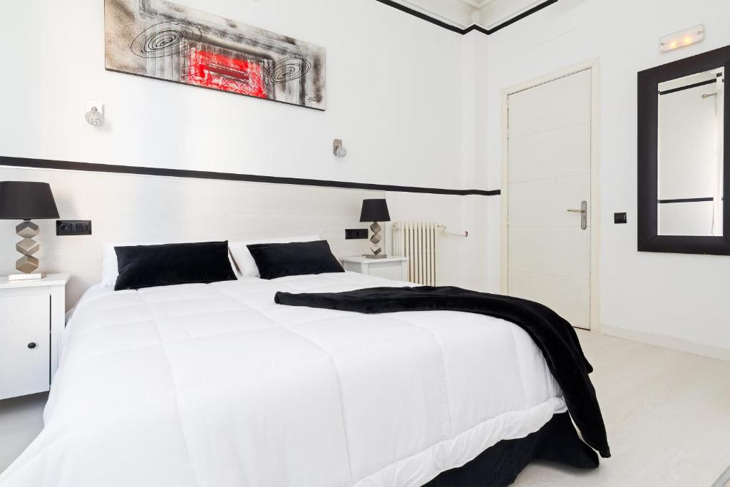 马德里63号大道旅馆的白色的卧室配有一张白色的床,上面有黑色毯子