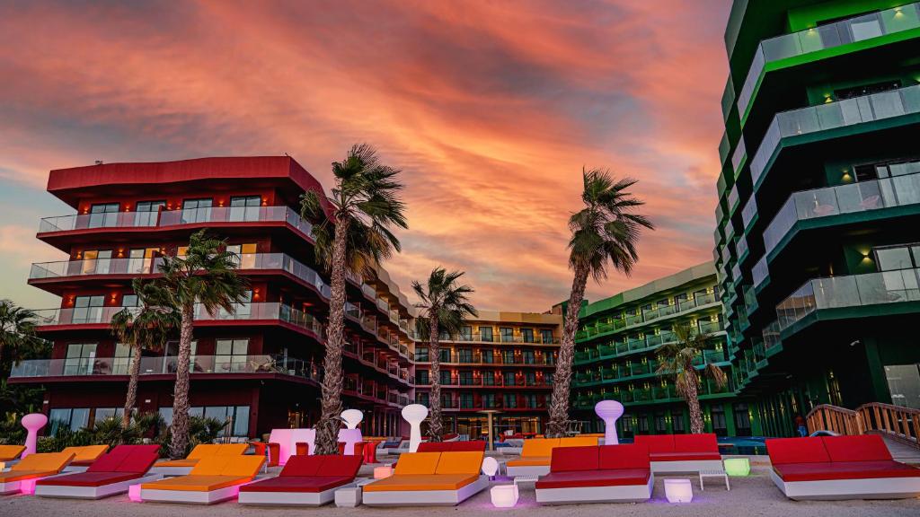 迪拜voco Monaco Dubai, an IHG Hotel, Adults Only, World Islands的一座棕榈树和椅子的建筑,位于一座建筑前