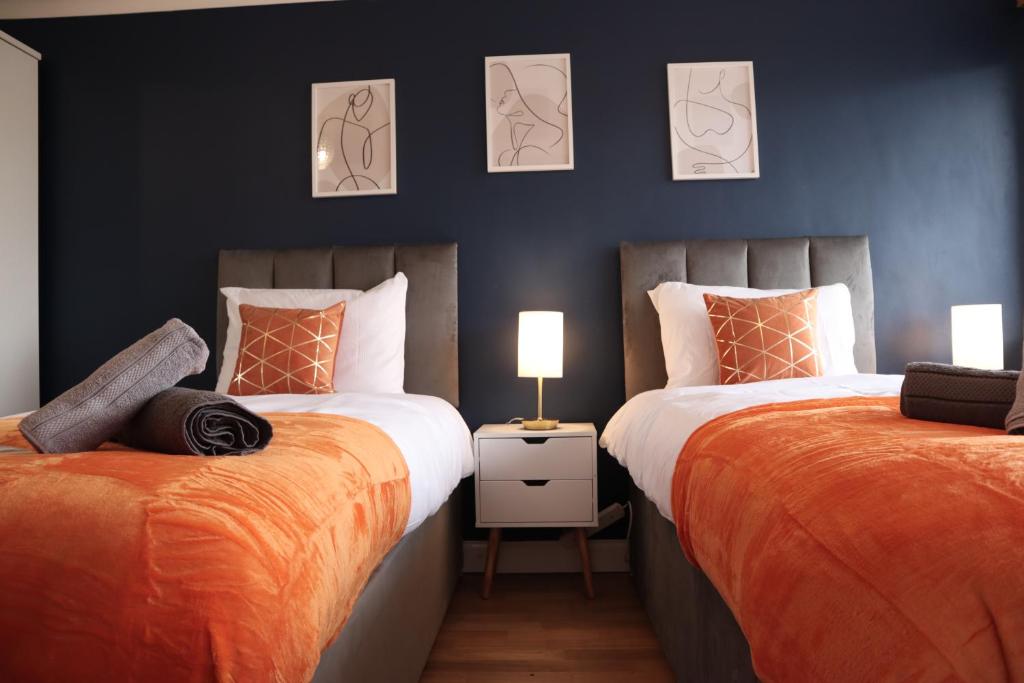 谢珀顿Perfect 2 Bedroom Flat Heathrow, Free Parking的一间卧室配有两张带橙色床单和两盏灯的床。