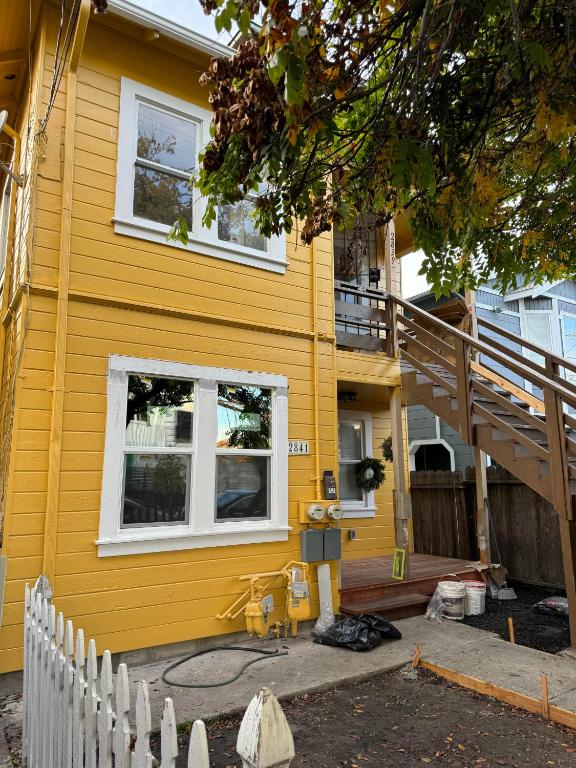 奥克兰Bumblebee House的黄色的房子,有白色的窗户和楼梯