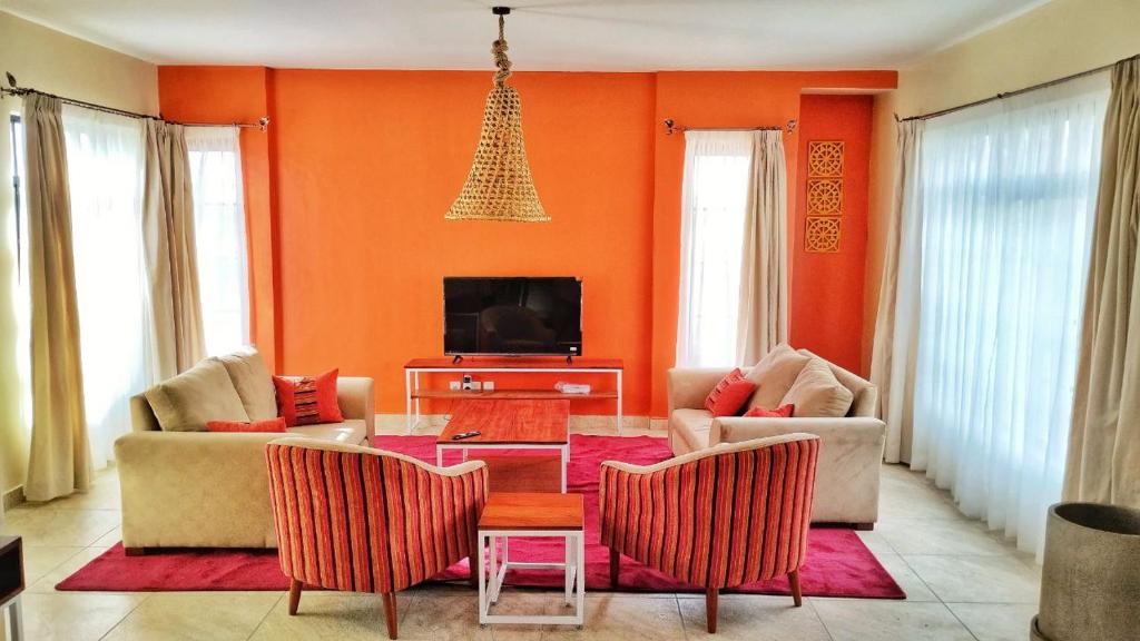 纳纽基Swara Ranch Nanyuki的客厅设有橙色墙壁和桌椅