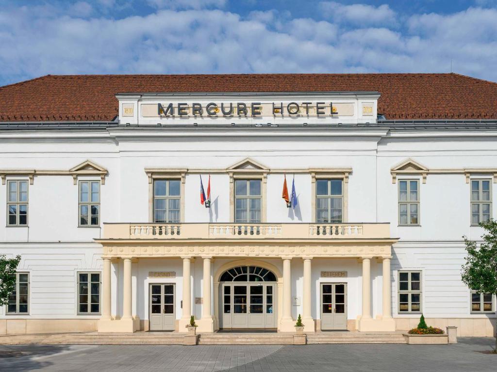 塞克希费黑瓦尔Mercure Szekesfehervar Magyar Kiraly的一座白色的大建筑,上面标有美化酒店的标志