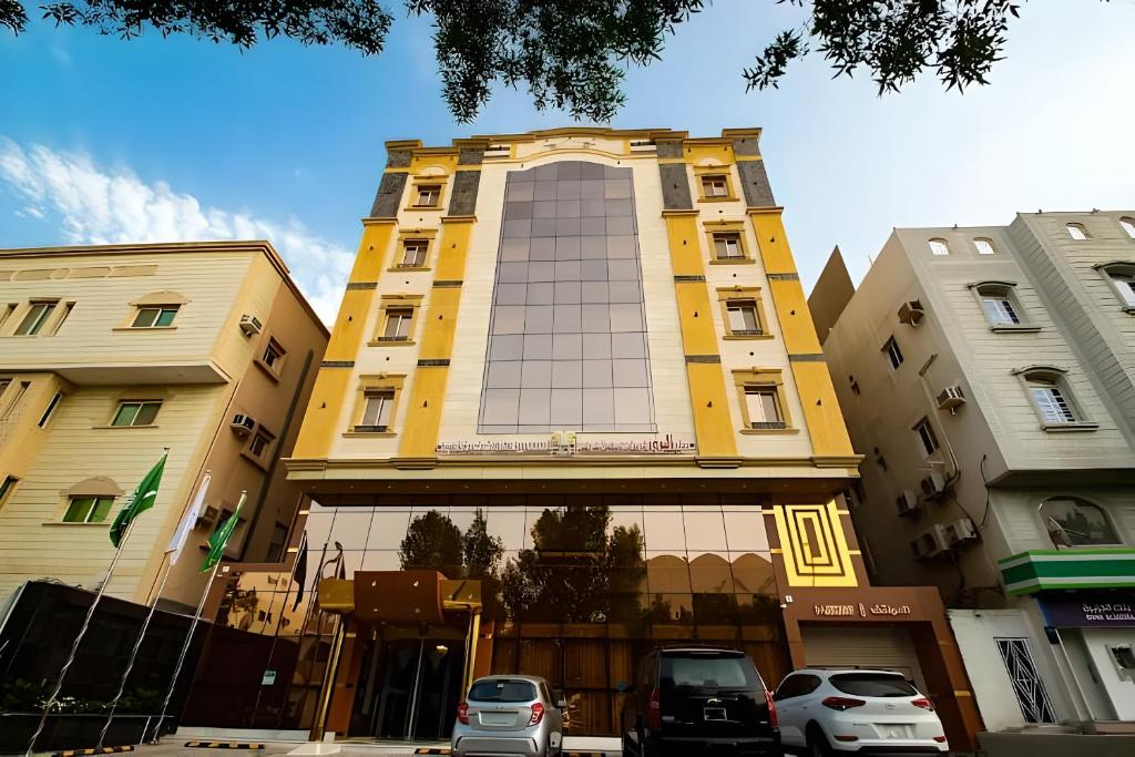 吉达Hayat Al Rose Hotel Appartment的一座黄色的建筑,前面有汽车停放