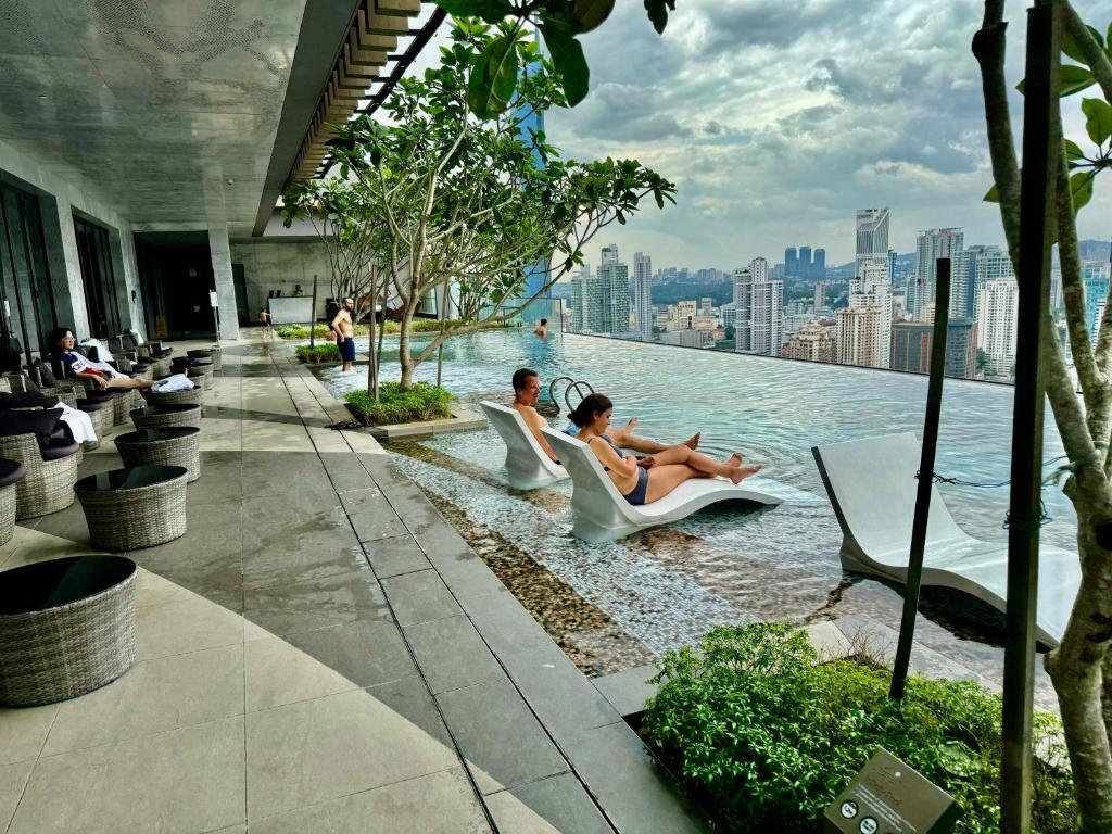 吉隆坡Axon Residence By Classy 1 minutes Pavilion的一座游泳池,里面的人坐在椅子上,位于一座建筑物的边缘
