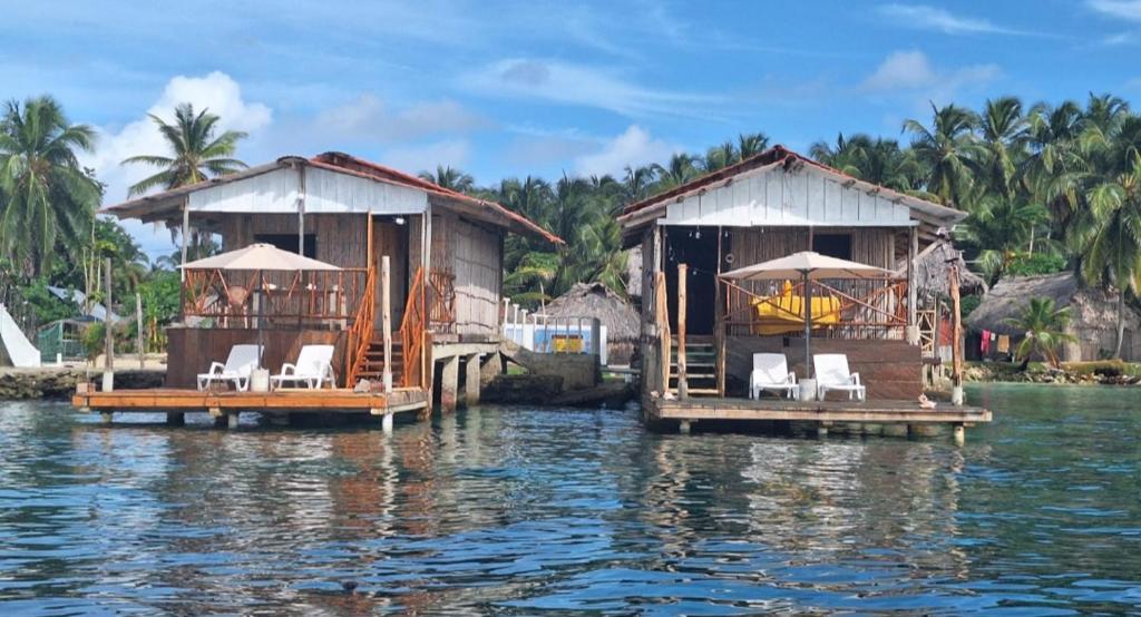 NusatupoCabañas sobre el mar en San Blas Narasgandub.的两栋水面房屋,配有椅子和遮阳伞