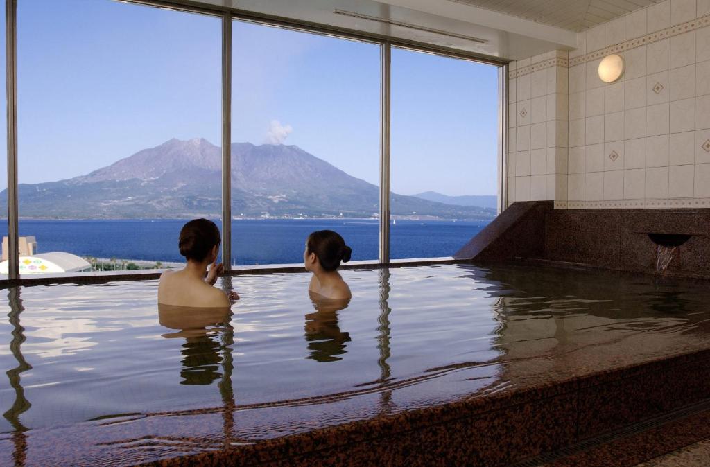 鹿儿岛鹿儿岛太阳皇家酒店的两个女人坐在游泳池里,望着水面