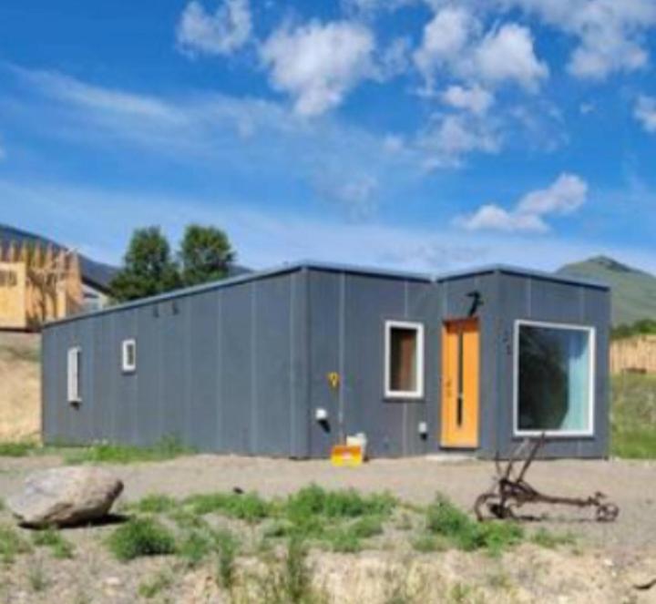 SalmonKarKens Container Home的一座灰色的小房子,田野上有一扇橙色的门