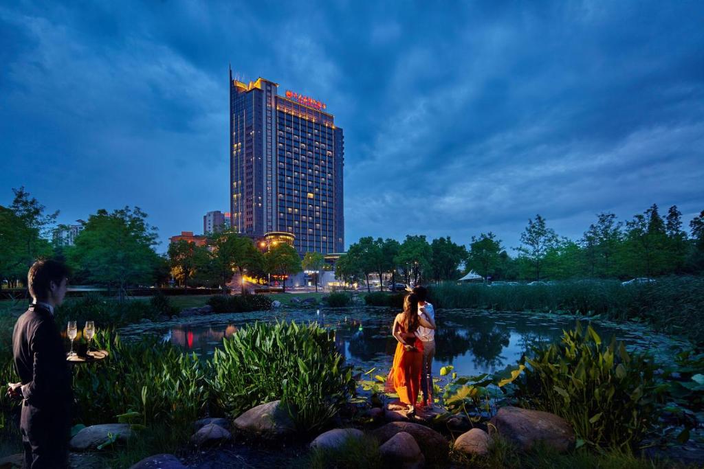 松江上海松江开元名都大酒店的一对夫妇站在池塘前,有一栋建筑