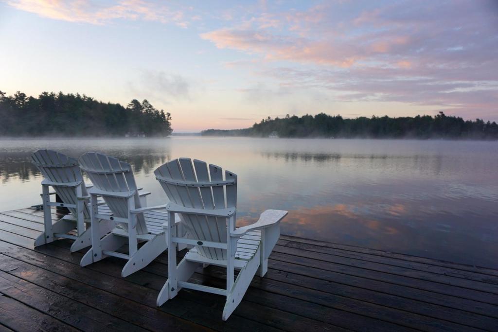 米内托Cozy Muskoka 4-bedroom cottage on Lake Rosseau的三个白色椅子坐在靠近水面的码头上