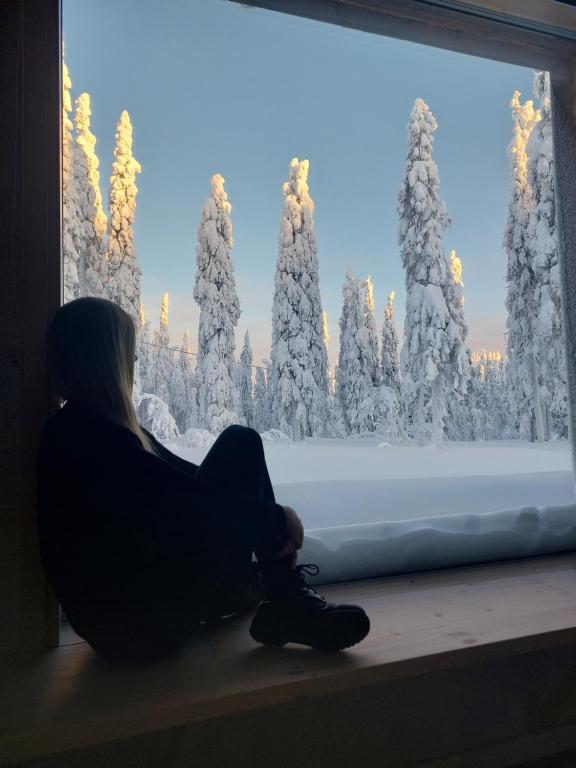 KotilaArctic Nest的坐在窗边的女人,看着雪覆盖的森林