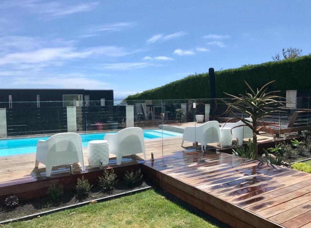 基督城Luxury 2 Bdrm Apt w Private Pool located on Scarborough Hill, Sumner. Christchurch的一个带白色椅子的甲板和游泳池