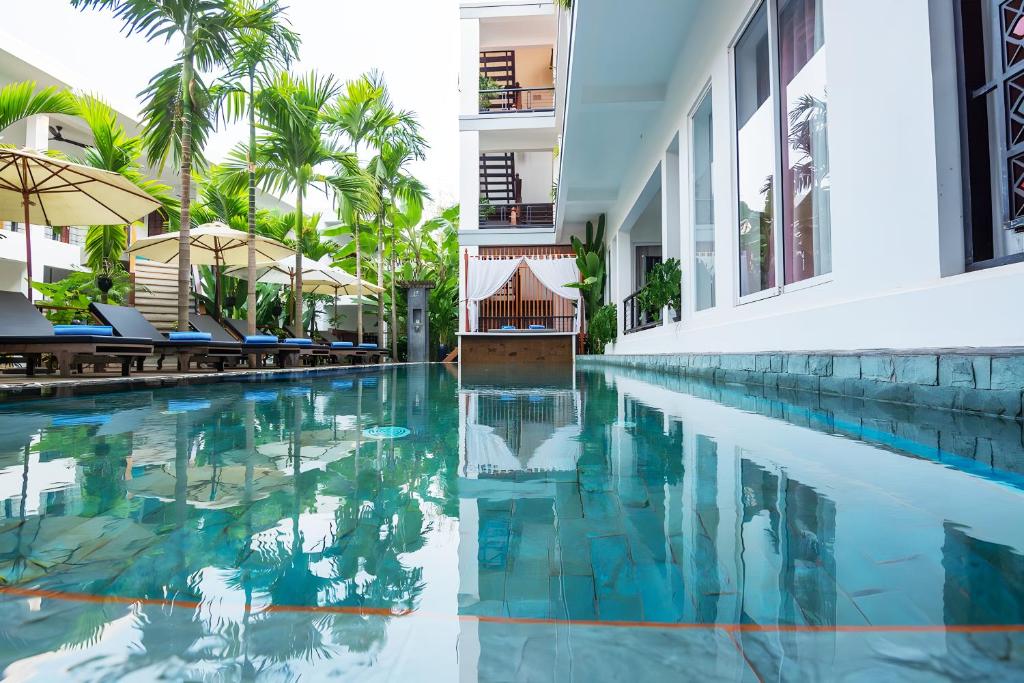 暹粒SAKABAN Suite的棕榈树建筑旁边的游泳池