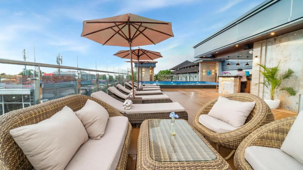 登巴萨City of Aventus Hotel - Denpasar的庭院设有藤椅和桌子以及遮阳伞。