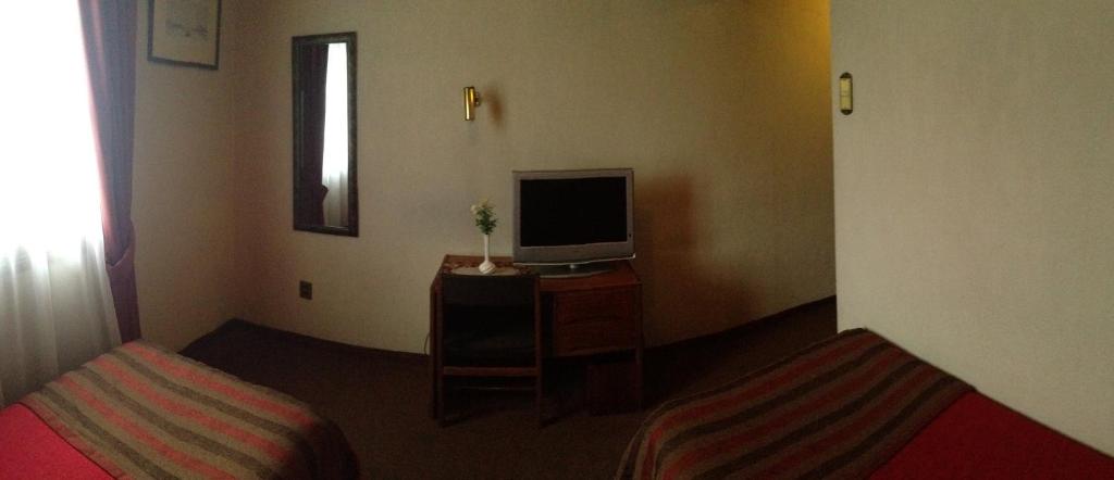 蓬塔阿雷纳斯默库里奥酒店的一间设有两张床和一张桌子上的电视的房间