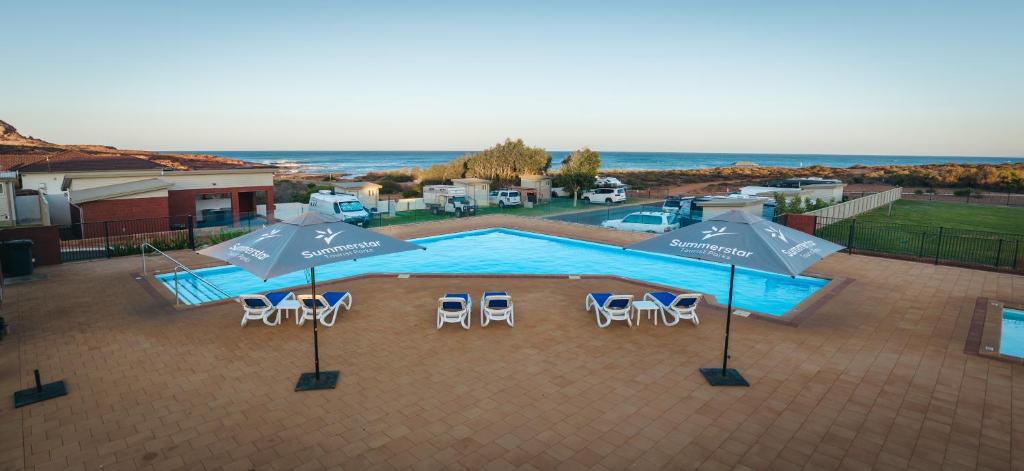 卡尔巴里Kalbarri Red Bluff Tourist Park的享有带遮阳伞和椅子的游泳池的顶部景致