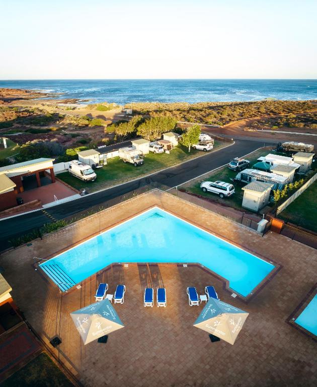 卡尔巴里Kalbarri Red Bluff Tourist Park的享有带椅子的游泳池和大海的顶部景致
