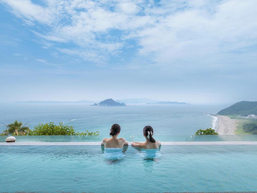 田原市Irago Ocean Resort的两个女人坐在一个无边游泳池里,望着大海